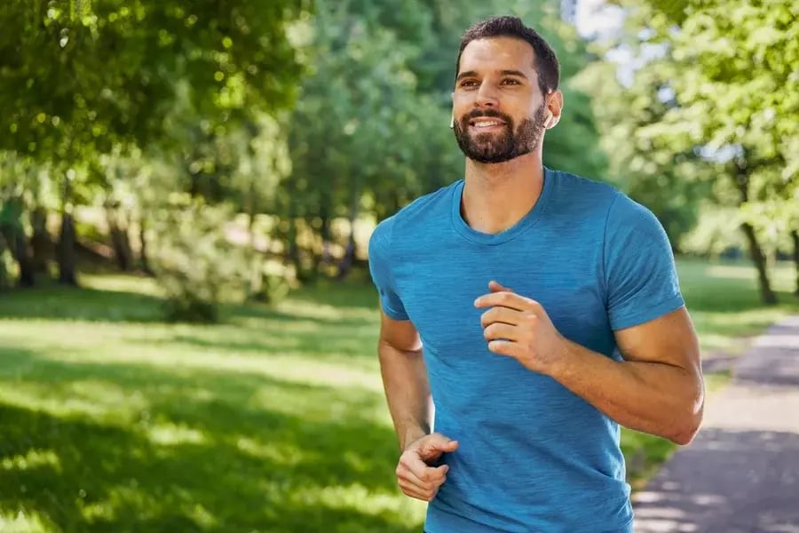 A man smiling as he jogs through the park.