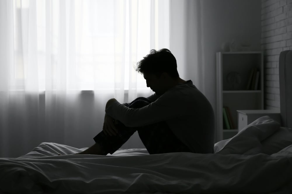 The silhouette of a young man, depressed, in bed.