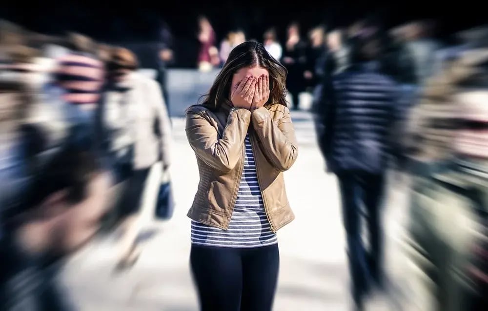 A woman experiencing anxiety, with her head in her hands, against a chaotic background.