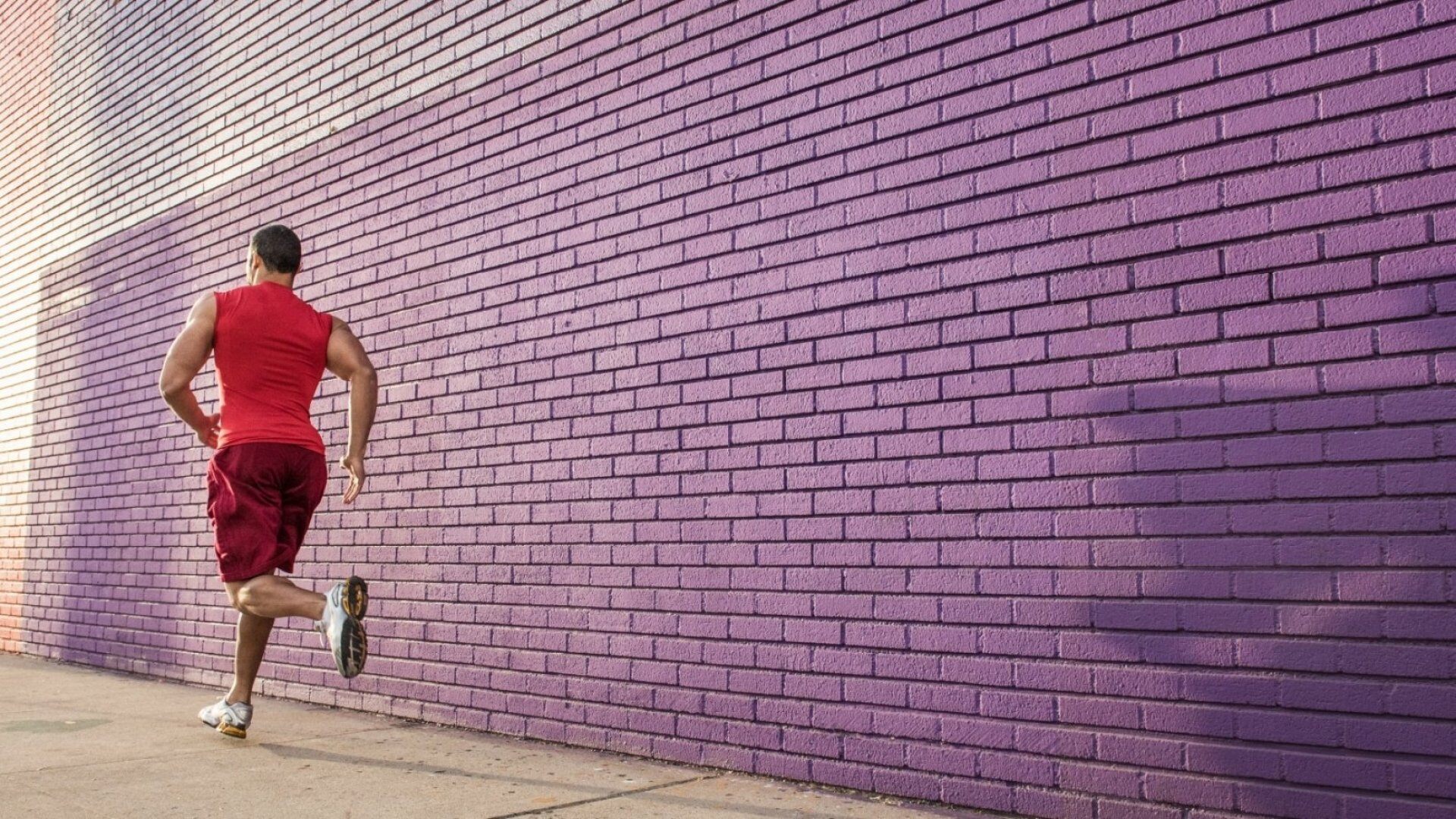 Rear view of male runner running along sidewalk
